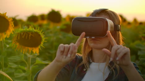 The-girl-farmer-manager-with-long-hair-in-plaid-shirt-and-jeans-is-working-in-VR-glasses.-She-is-engaged-in-the-working-process.-It-is-enjoyable-sunny-evening-in-the-sunflower-field-at-sunset.